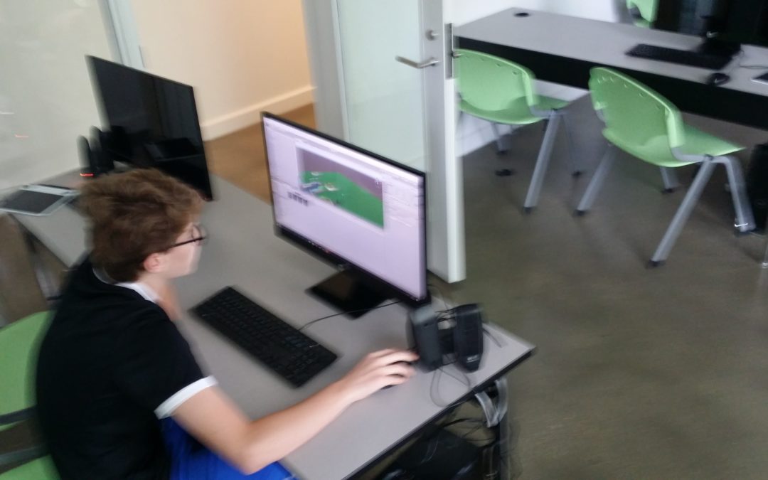 A young student sitting at a desk programming a game.