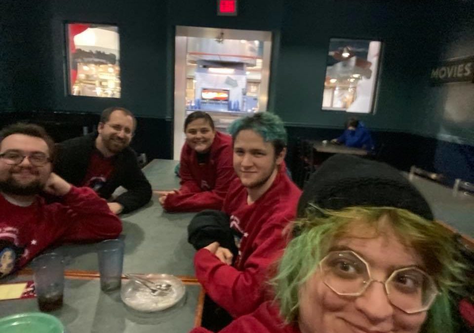 A bunch of people sitting at a green formica table wearing matching red sweatshirts
