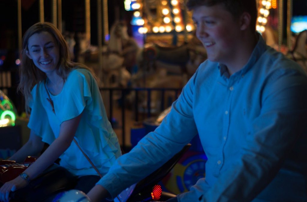 A young man and woman, illuminated blue, playing at the arcade.